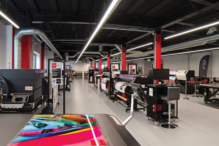 The Hybrid Services showroom featuring grey concrete floor and red painted pillars. The room is filled with wide-format printers