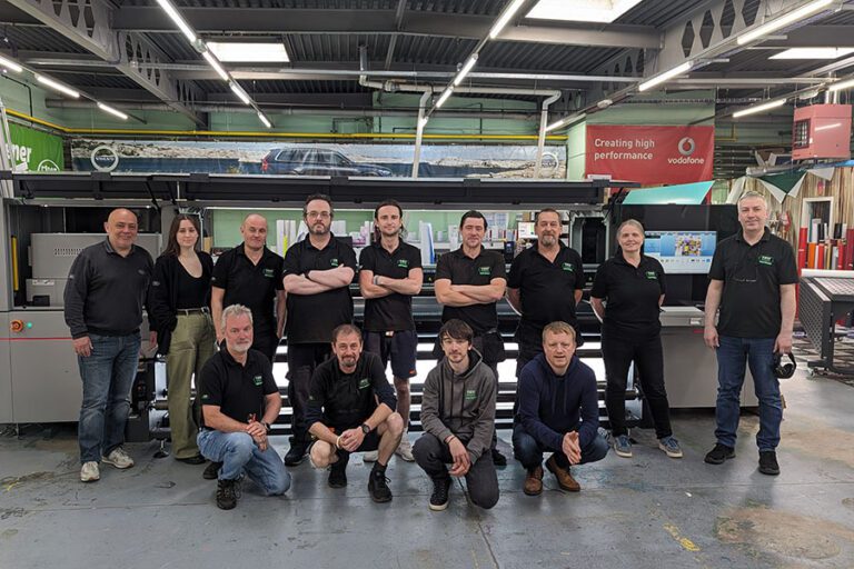 The First Display Signs & Graphics team in front of a wide-format printer in a print warehouse