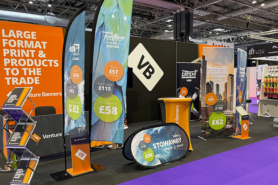 Venture Banners' stand at The Print Show, showcasing its range of flags and banners with a purple floor in the foreground