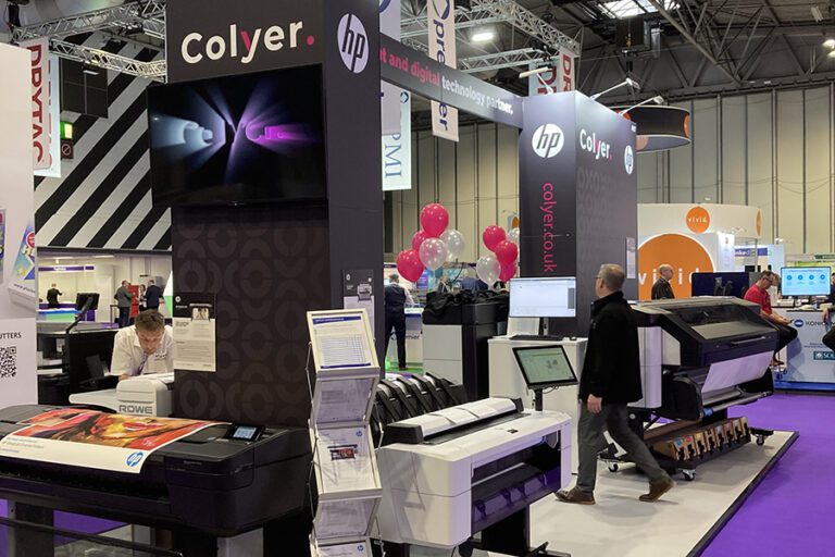 Colyer's stand at The Print Show last year, the stand features a HP printer in front of black graphics with the colyer logo on it