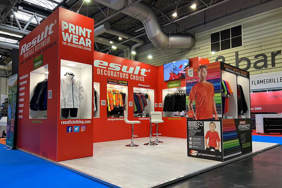 An image of the Result Clothing stand at a previous trade show. The stand is bright red and is demonstrating a range of fleeces and other jumpers that can be printed on